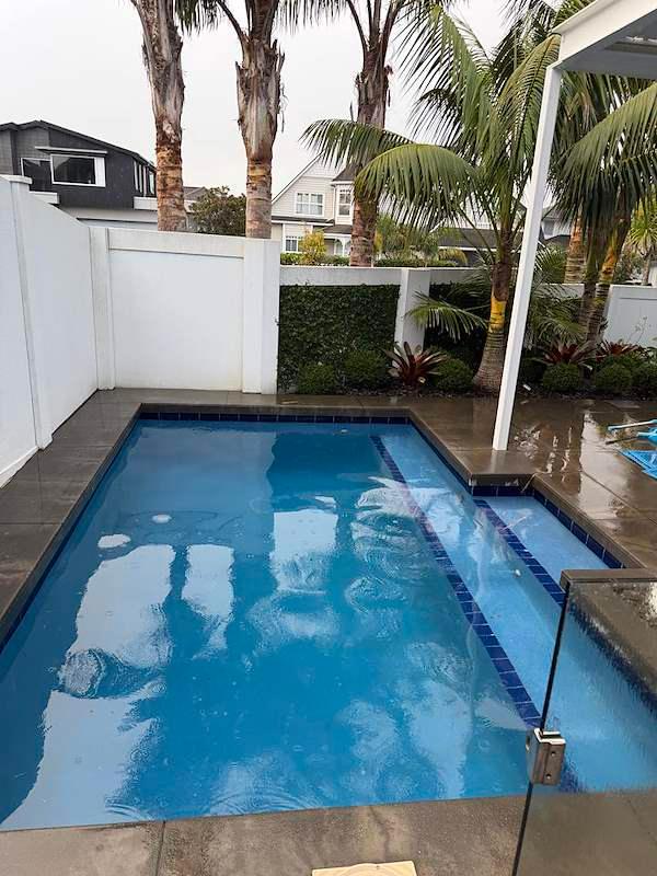 Rectangular pool with a raised spa, blue tiled edge, and white privacy fencing