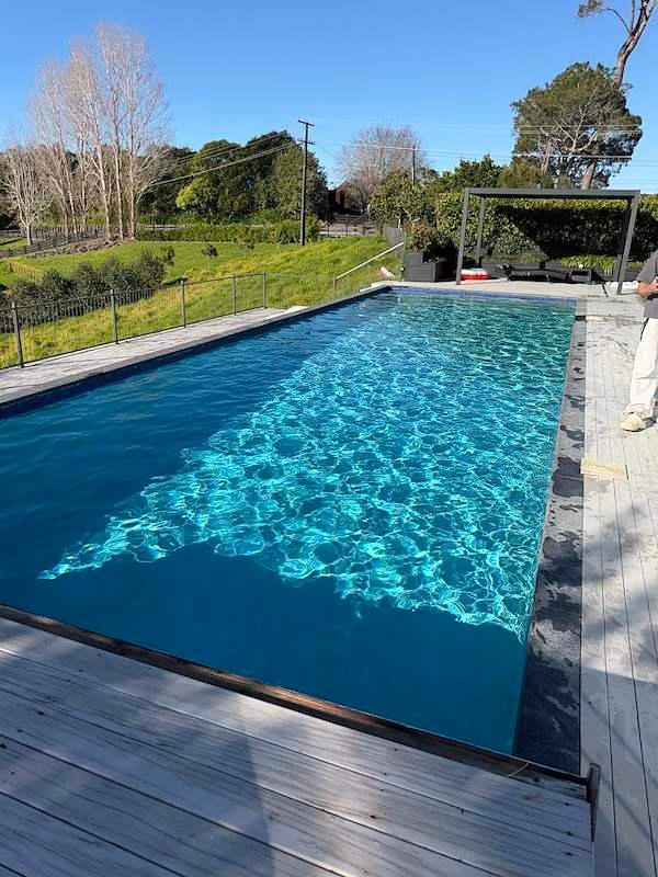 Long lap pool with a timber deck and pergola overlooking open countryside